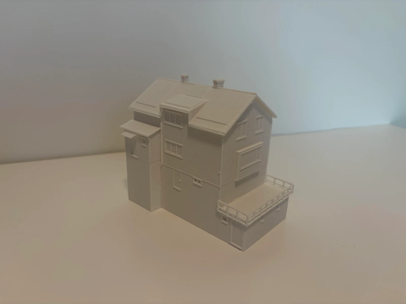 En fysisk, vit 3D-printad husmodell med tak, fönster och terrass